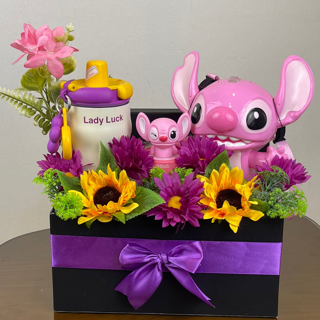 Tagerelsa3ada Angel and Stitch gift box with pink Angel figure, mini Stitch, Lady Luck sippy cup, sunflowers, purple daisies, and greenery in a black box with purple ribbon.