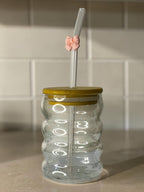 Tagerelsa3ada clear glass tumbler with a ribbed design, bamboo lid, and a clear straw adorned with a small pink bow.