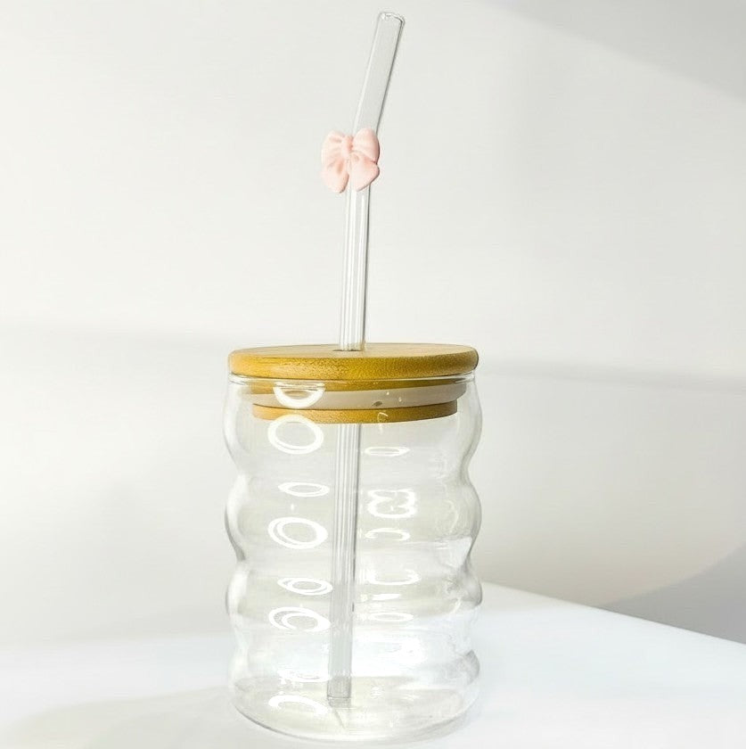 Tagerelsa3ada clear glass tumbler with wavy design, bamboo lid, and glass straw adorned with a pink bow.