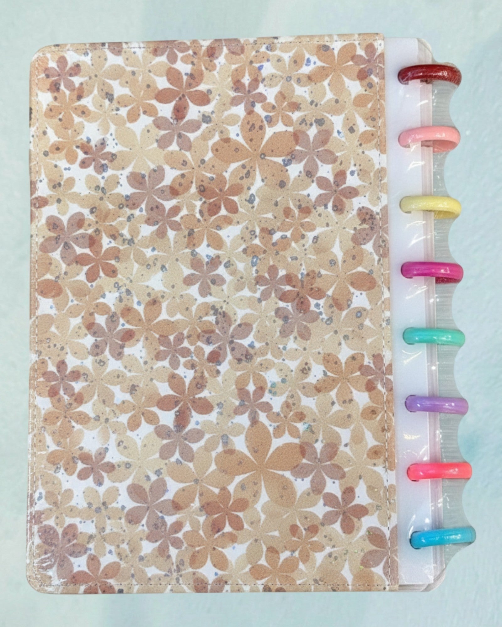 Tagerelsa3ada floral discbound planner with a beige and brown all-over flower print and colorful disc binding.