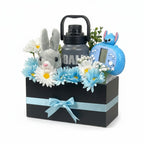 Tagerelsa3ada grey plush bunny, blue and white daisies, grey water bottle, and blue toy in a black gift box with a light blue ribbon.
