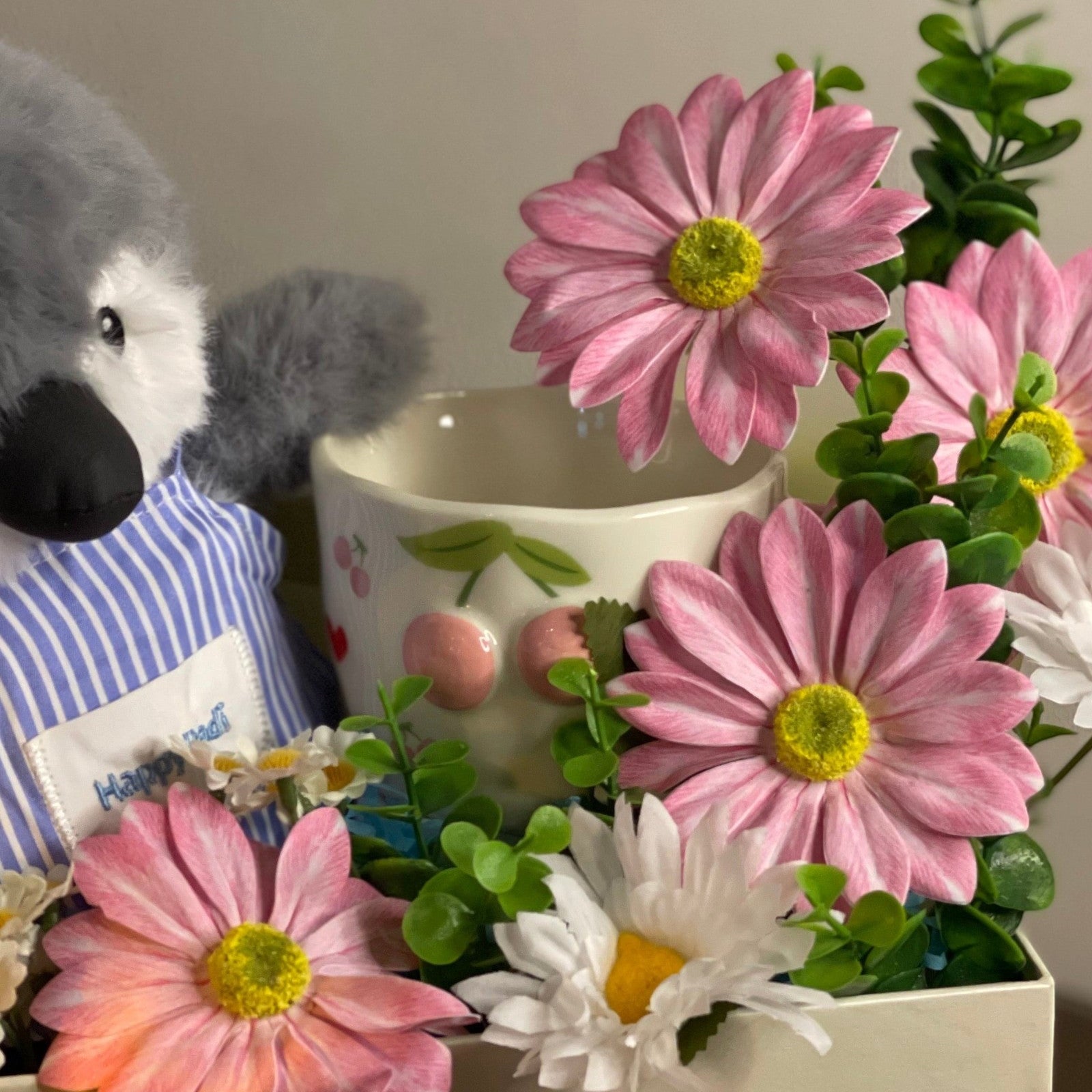 Tagerelsa3ada plush penguin chef in blue striped shirt with pink and white daisies and greenery in a cream box.