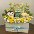 Tagerelsa3ada Penguin and Stitch gift box with plush penguin, Stitch figurine, mug, yellow roses, daisies, and decorative foliage in a cream box with blue ribbon.