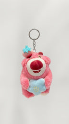 Tagerelsa3ada pink plush bear keychain holding a blue star with embroidered flowers, wearing a strawberry hat.