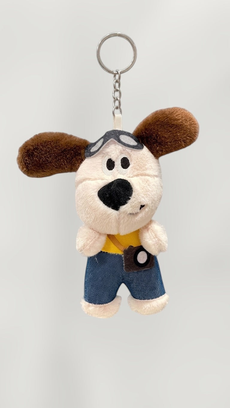 Tagerelsa3ada plush dog keychain with aviator goggles and camera accessory, wearing denim shorts and yellow shirt.