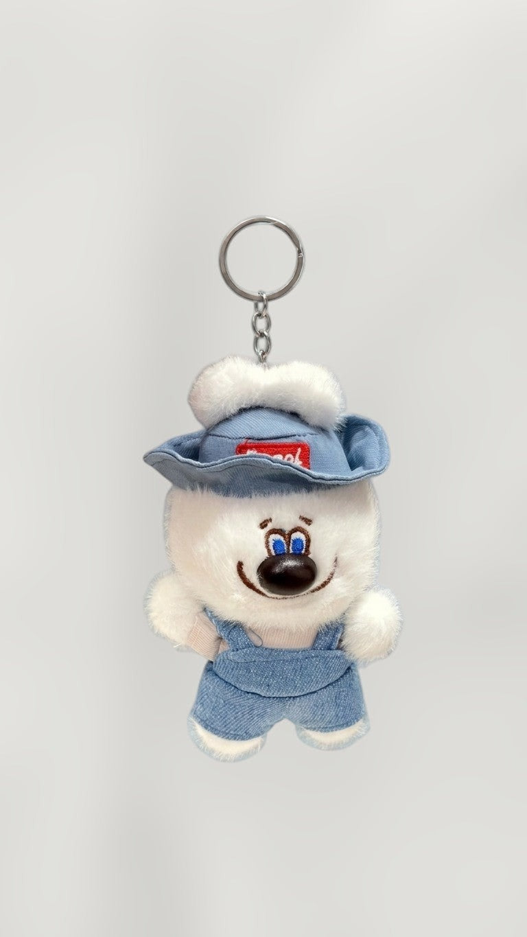Tagerelsa3ada plush dog keychain with blue denim overalls, white trim, and a blue hat with white pompom. Features a camera accessory.