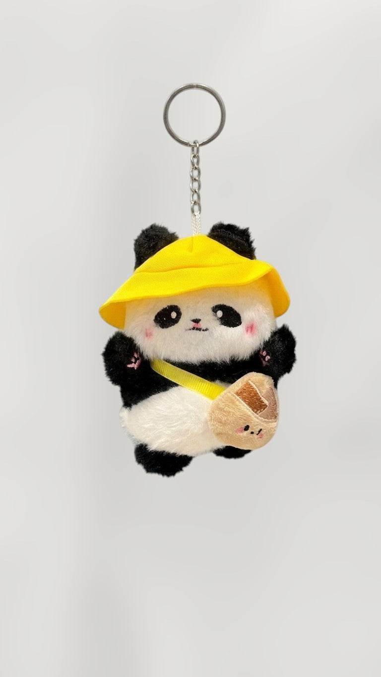 Tagerelsa3ada plush panda keychain wearing a yellow hat and carrying a small bag, with a yellow strap across its body.