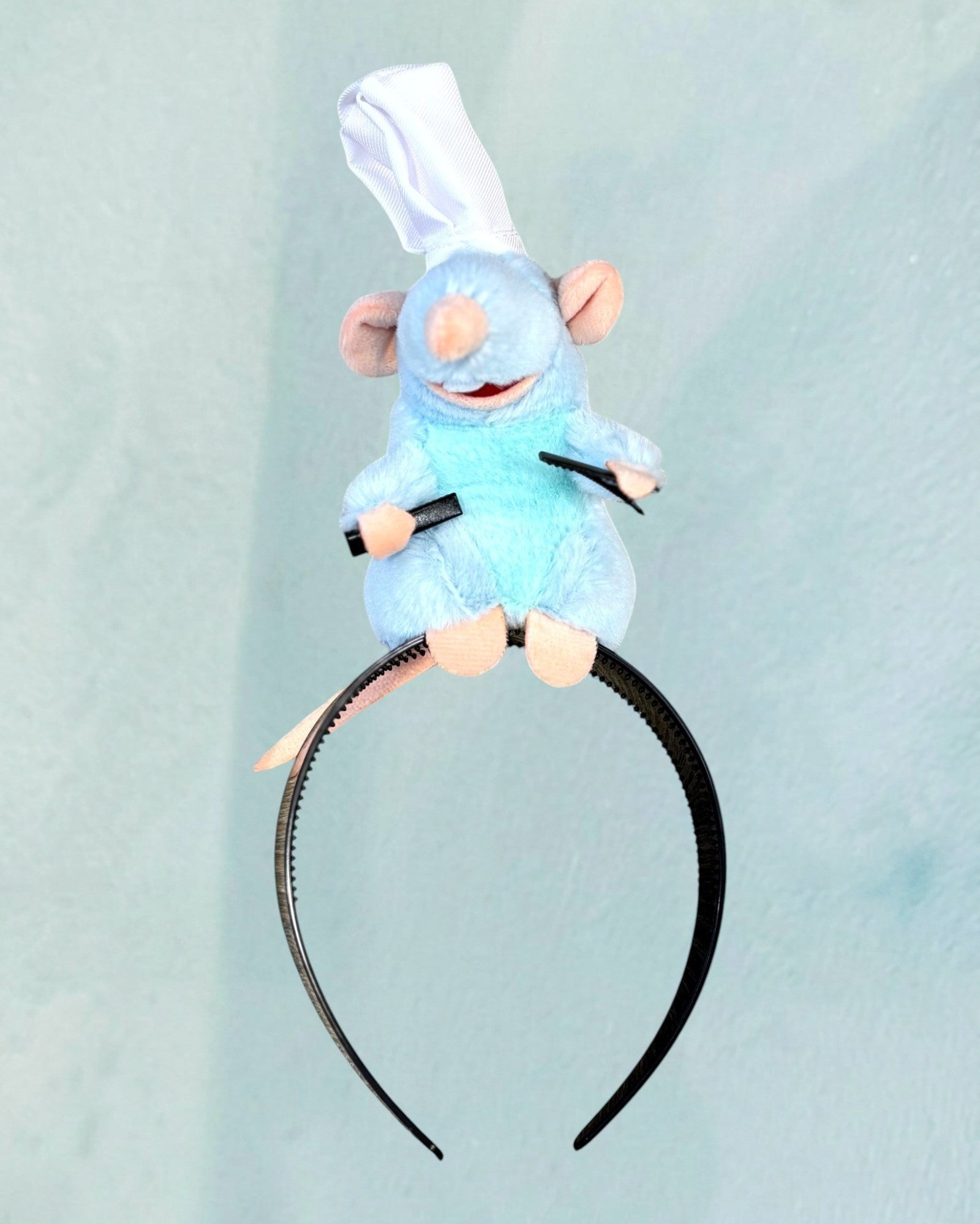 Tagerelsa3ada blue plush rat character headband with chef hat and embroidered details, holding black utensils.