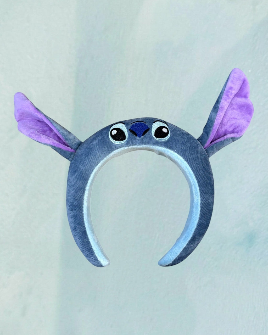 Tagerelsa3ada blue plush Stitch character headband with purple ears and embroidered face details.