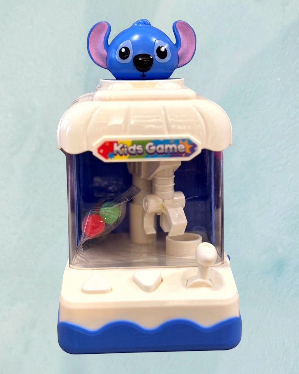 Tagerelsa3adaHere blue and white mini kids game claw machine toy with a blue character on top and colorful prizes inside.