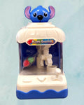 Tagerelsa3adaHere blue and white mini kids game claw machine toy with a blue character on top and colorful prizes inside.